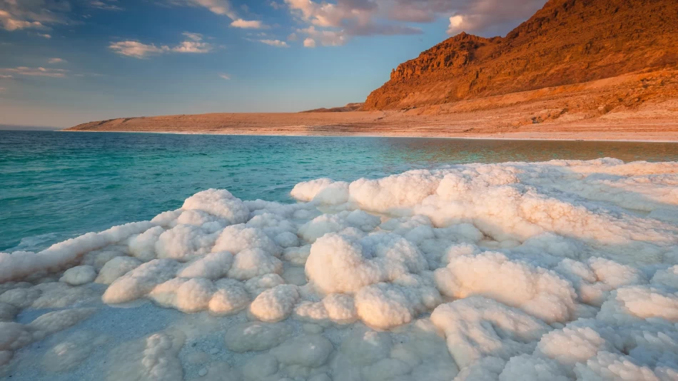 Calm turquoise waters of the Dead Sea in Jordan, surrounded by salt formations and desert mountains.