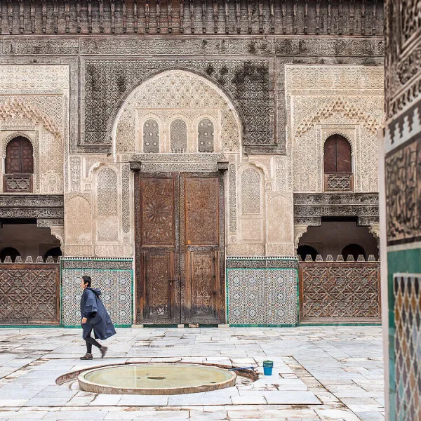 Courtyard of Bou Inania Madrasa in Meknes with zellige tiles, carved wood, and a central fountain