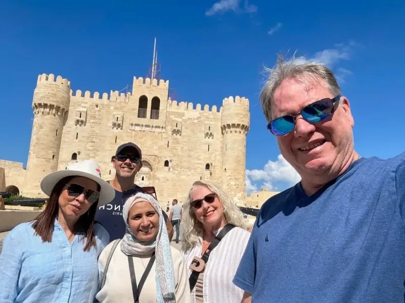 A group of travelers taking a selfie in front of the Qaitbay Citadel in Alexandria